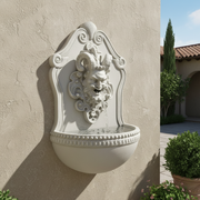 Wall-mounted fountain with ornate Baroque face motif, classical scrollwork, and old world European decorative detailing. Side Angle