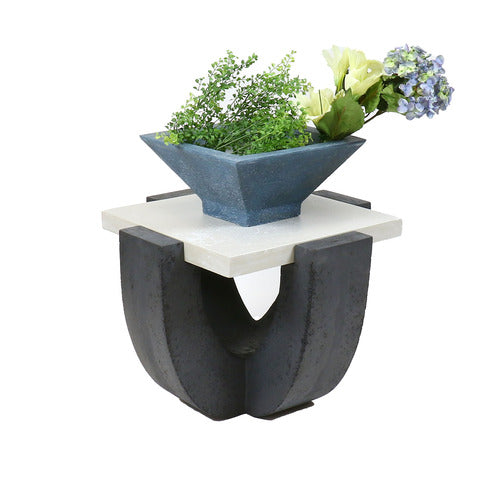 Square side table with a classical, old world European base and ornate geometric design, topped with a decorative floral arrangement.