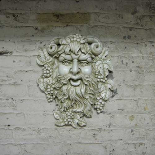 Grotesque bearded face with ram horns, grape clusters, and ornate leaves in an old world European classical style. Side Angle