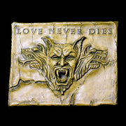Baroque-style ornate plaque featuring a fierce, snarling gargoyle face with three wolf heads and "Love Never Dies" inscription above. Side Angle