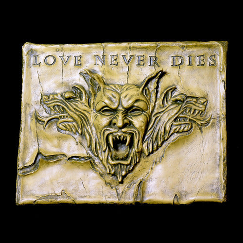 Baroque-style ornate plaque featuring a fierce, snarling gargoyle face with three wolf heads and "Love Never Dies" inscription above. Side Angle