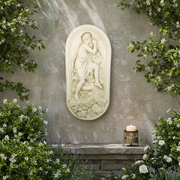 Relief sculpture of a classical figure playing a flute, draped in robes, set against an ornate old world European background. Side Angle