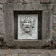Baroque-style wall plaque featuring an ornate, classical face with flowing hair, grape clusters, and dramatic expression. Side Angle