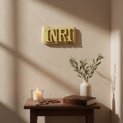 INRI plaque with bold, classical raised lettering on an ornate, scroll-shaped background in old world European style. Side Angle