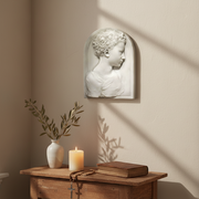 Classical Renaissance-style bas-relief of a young child in profile with ornate, curly hair and arched background panel. Side Angle