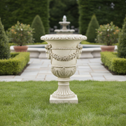 Ornate classical urn with ram head accents, laurel garland, and fluted pedestal in old world European Baroque style. Side Angle