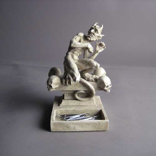 Grotesque horned demon statue in medieval Gothic style, crouching on a pedestal adorned with ornate skull details. Side Angle