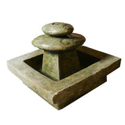 Tiered old world European fountain with stacked rounded forms and square basin, featuring a simple, classical architectural style.