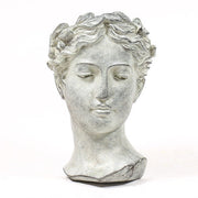 Classical Greek-style bust of a serene female figure with ornate, wavy hair and softly defined facial features.