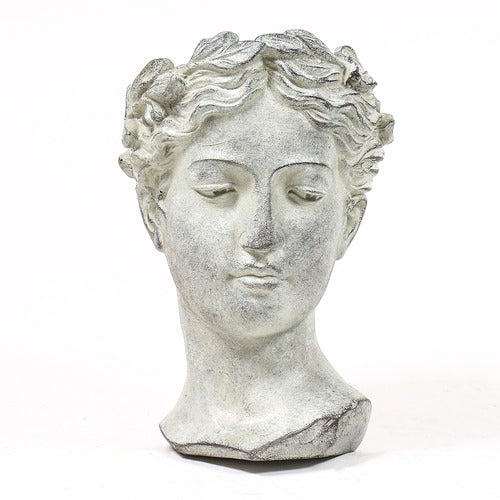 Classical Greek-style bust of a serene female figure with ornate, wavy hair and softly defined facial features.