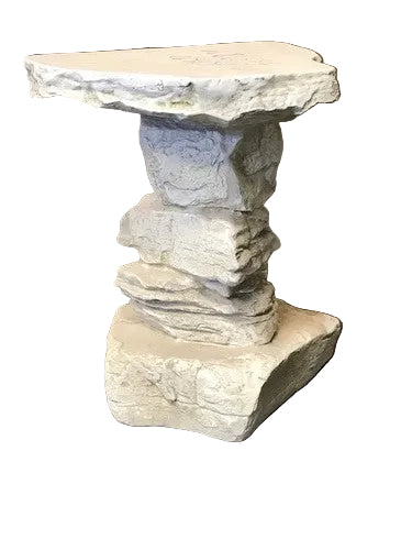 Stone pedestal table with stacked, rough-hewn base and irregular top, evoking old world European and medieval architectural style.