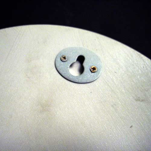 Keyhole escutcheon plate with two screws on a smooth, rounded surface, featuring simple, classical design elements. Side View
